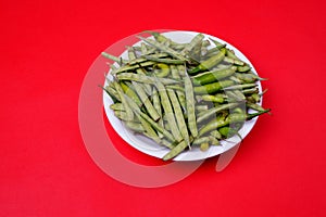 Closeup shot of green beans and chili pepper on plate isolated on red background