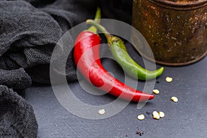 Closeup shot of the green and red hot chili peppers with cloth on a dark tabletop