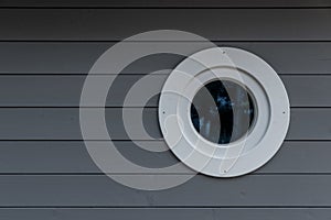 Closeup shot of a grey wooden wall with a small wooden white porthole