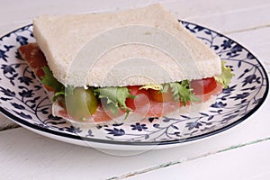 Closeup shot of a ham sandwich on a white plate with blue flowers on it