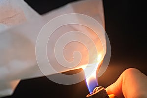 Closeup shot of a hand burning a paper with fire flames in a blurred background