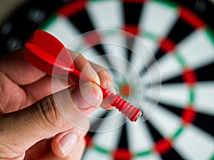 Closeup shot of a hand holding a red dart in front of a dartboard