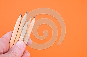 Closeup shot of a hand holding wooden pencils isolated on an orange background