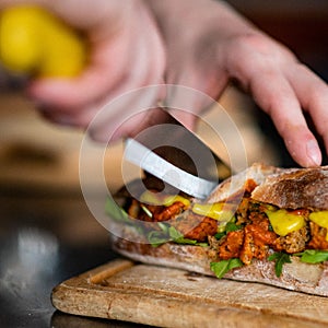Closeup shot of hands cutting a vegan sandwich with a knife