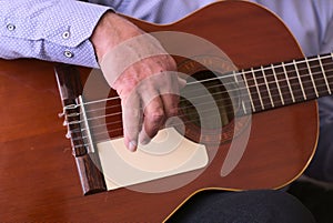 Closeup shot of the hands of a senior male playing guitar while sitting on the couch
