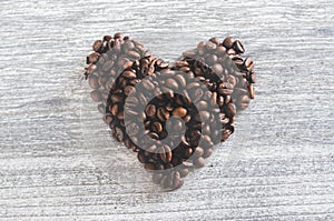 Closeup shot of a heart-shaped figure with coffee beans on a wooden background