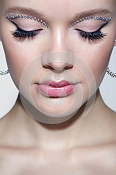 Closeup shot of human female face with unusual rhinestones makeup. Woman with closed eyes and earrings in the form of a shiny ring