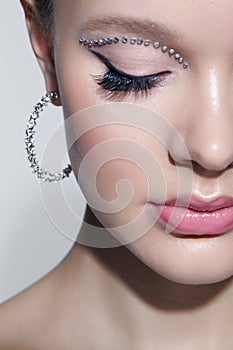 Closeup shot of human female face with unusual rhinestones makeup. Woman with closed eyes and earrings in the form of a shiny ring