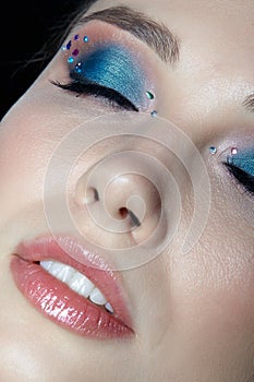 Closeup shot of human woman face with eyes closed and beauty makeup with blue eye shadow make up and rhinestones