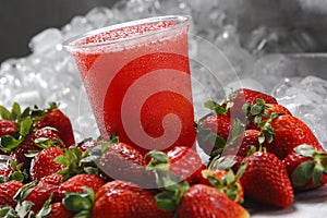 Closeup shot of icy strawberry smoothie in a plastic cup on background of ice cubes and strawberries