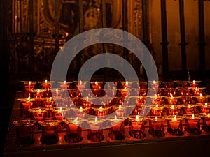 Closeup shot of lit votive prayer candles in a church in front of a Saint Mary statue