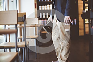 Closeup shot of a male holding his coffee and the bible while standing near a wooden table