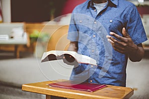 Closeup shot of a male reading the bible near a wooden stand with a blurred background