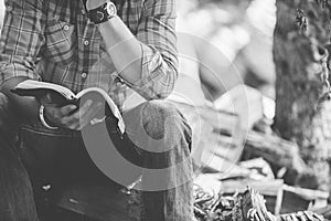 Closeup shot of a male sitting on the ground while reading the bible with blurred background