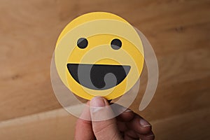 Closeup shot of a man holding a laughing smiley face sign on a wooden background