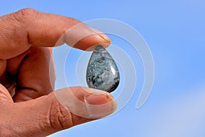 Closeup shot of a man holding a teardrop shape stone with a clear blue sky in the background