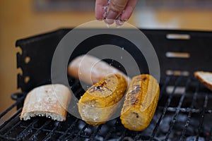 Closeup shot of man salting corn grilled next to bread on the grates