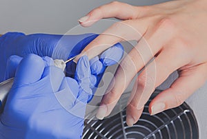 Closeup shot of manicurist in blue rubber gloves cleans cuticle on female nails using a milling cutter for manicure