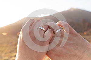 Closeup shot of a married couple hands with silver wedding rings on a sunny day