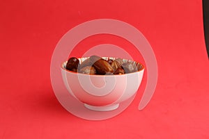 Closeup shot of medjool dates in a white bowl on a red background