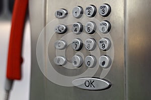 Closeup shot of a metal payphone keypad with red phone