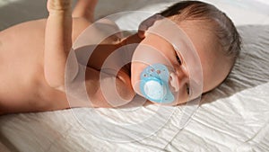 Closeup shot of mother giving soother to her newborn baby son lying on bed in sun rays