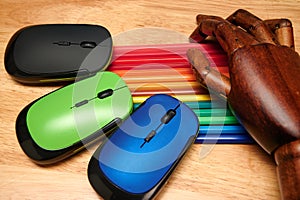 Closeup shot of multi-colored pencils, computer mouses with an articulated wooden hand