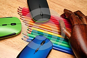 Closeup shot of multi-colored pencils, computer mouses with an articulated wooden hand