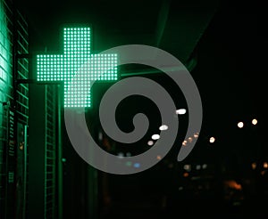 Closeup shot of a neon green cross light signage hanging from a wall at night in a city