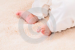 Closeup shot of newborn baby`s feet, wearing bodysuit with diaper comfortable lying at home, newborn chubby leg bodypart movement