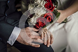 Closeup shot of a newly married couple holding hands with a flower bouquet