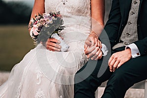 Closeup shot of a newly-wed couple sitting on a bench holding hands with each other