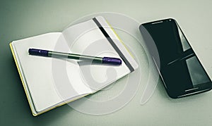 Closeup shot of a notebook with a grey and purple pen on it next to a phone
