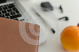 Closeup shot of a notebook planner on a laptop with orange fruit on a table