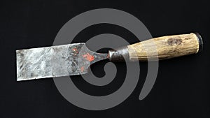 Closeup shot of an old rusty chisel with wooden handle isolated on a black background