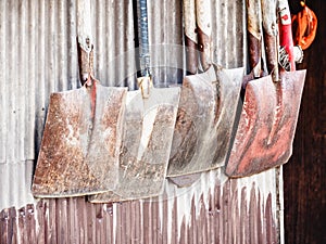 Closeup shot of old rusty shovels hanging on a metallic wall