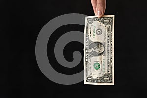 Closeup shot of one dollar bill held by a pair of fingers on a black background