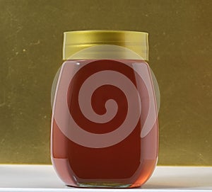 Closeup shot of one full glass honey jar on a blur golden Background