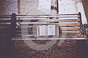 Closeup shot of an open bible on a wooden bench with a blurred background