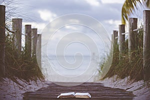 Closeup shot of an open bible on a wooden pathway towards the beach with a blurred background