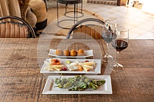 Closeup shot of Padron peppers, Plateau Fromage, and Arancini balls served with two wine glasses