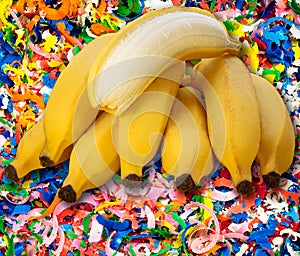 Closeup shot of a partially peeled banana on a bundle of bananas on colorful crayon shavings