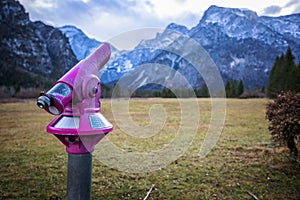 Closeup shot of a partially rusty long-distance watcher in a park in front of rocky mountains