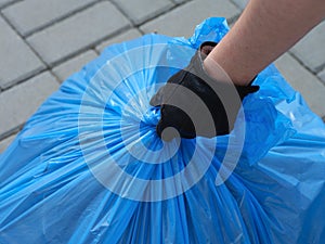 A closeup shot of a person hand taking a blue garbage bag full of trash