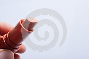 Closeup shot of a person holding a beige lipstick isolated on a grey background