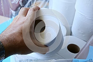 Closeup shot of a person holding a roll of toilet paper over a pile of toilet papers