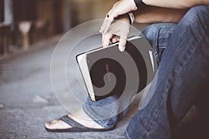 Closeup shot of a person sitting on the ground while holding the bible with a blurred background