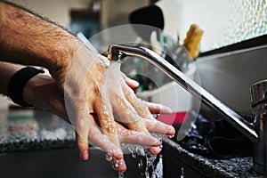 Closeup shot of a person washing hands in the sink in the kitchen