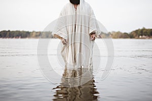 Closeup shot of a person wearing a biblical robe standing in the water with a blurred background
