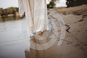 Closeup shot of a person wearing a biblical robe walking on the shore with a blurred background